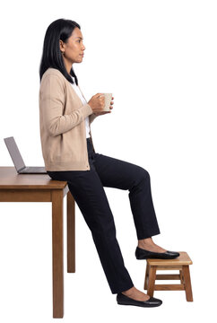 Woman Sitting on Desk Drinking Coffee Beside Laptop