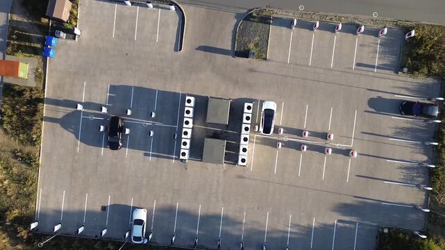 Danish EV charging park with multiple charging stations arranged along marked parking rows. Several cars are parked near the chargers, and surrounding grass areas frame the modern facility