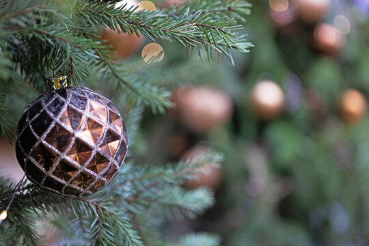 Dark metallic sphere with diamond facets hangs on green fir. Warm blurred lights create festive depth. Elegant Christmas decor. Background for New Year's or Christmas greetings. Copy space