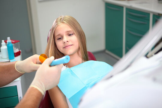 Blonde girl in dentist's chair. Dentist's gloved hands hold curing lamp. Modern office