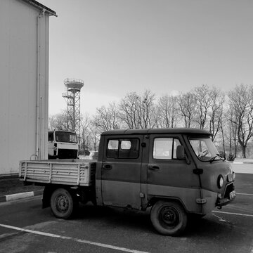 Black and white side view of an old double cab utility pickup truck parked on an asphalt lot near a building
