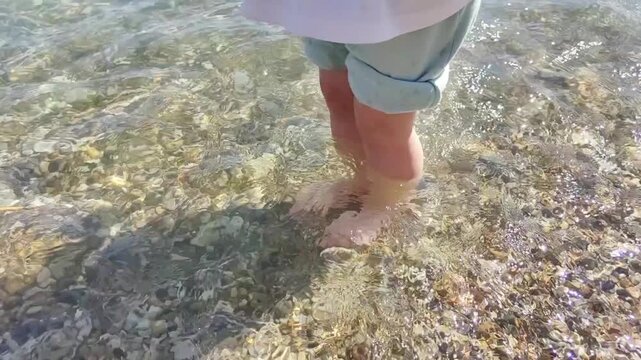 Child&rsquo;s feet stomping on pebbles in sea water to support sensorimotor development. Great for educational and therapy videos, parenting content, early childhood resources, wellness, travel promotions