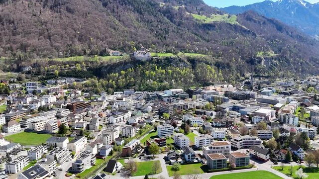 vaduz castle hillside cliff aerial view forested mountain slopes alpine peaks snowcapped town rooftops below vineyard terraces rhine valley liechtenstein drone footage establishing shot heritage site