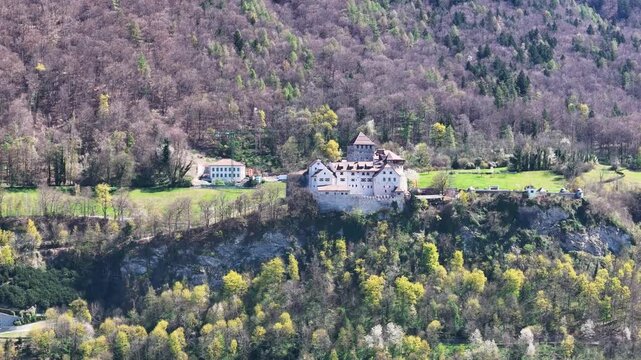 vaduz castle perched rocky cliff outcrop aerial close orbit stone walls tower turret gabled roofs forested hillside mountainside clearing liechtenstein drone footage heritage site medieval fortress