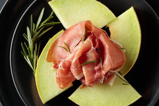 Italian prosciutto with melon and fresh rosemary on a black background.