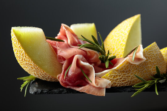 Sliced Italian prosciutto or Spanish jamon with melon and rosemary.