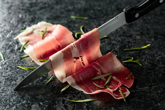 Sliced prosciutto and knife on a stone table.