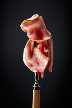 Raw fresh smoked pork bacon slices on a fork.
