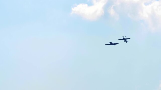 Propeller planes flying in formation against bright blue sky and white cumulus clouds during airshow, wide shot