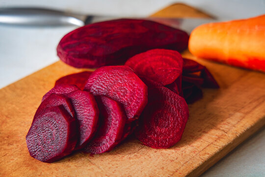 Sliced red beetroot on wooden cutting board with carrot behind