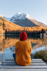 Fototapeta premium Person sitting on lakeside dock with mountain reflection and autumn trees for outdoor background and travel banner