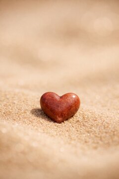 Small heart shaped stone on sandy beach minimal love background for romantic banner greeting card and wallpaper design