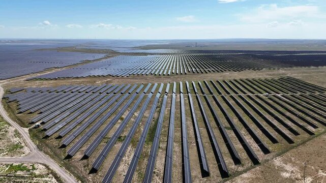 Aerial view of vast solar panel arrays on flat terrain under blue sky