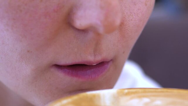 Young adult person sips coffee with focused expression in close up, tasting latte art in cafe setting and pausing between swallows. Coffee drinker stays near cup rim, suggesting coffee tasting.