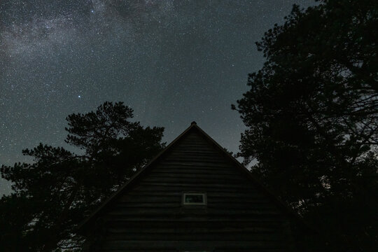 Wooden forest cabin roof silhouette under the Milky Way starry night sky in Omma raba bog landscape in Estonia.