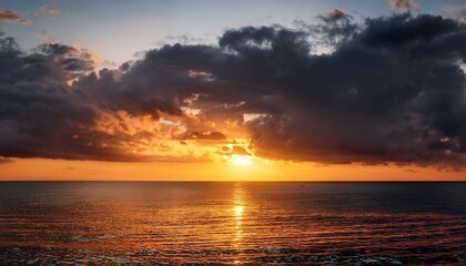 Fototapeta premium Dramatic Evening Sky Over The Sea The Setting Sun Hides Behind Heavy Dark Clouds Casting A Fiery Orange Reflection On The Calm Water Surface