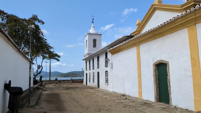 Paraty, Rio de janeiro: Slow motion static shot of Capela de Nossa Senhora das Dores church next to the beach, showing colonial architecture and green doors on an old street.