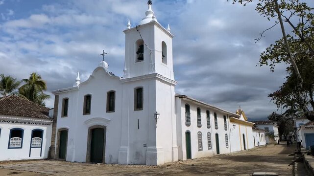Paraty, Rio de janeiro - 2026: Slow motion static view of the historic Capela de Nossa Senhora das Dores colonial church under a dramatic cloudy sky on a cobblestone square.