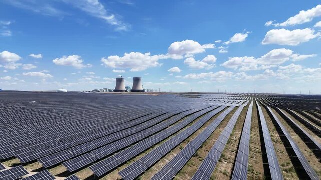 rows of solar panels under blue sky with cooling towers in background