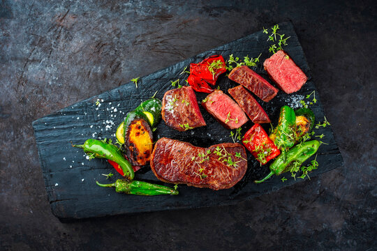 BBQ broiled gry aged roastbeef with roasted vegetable served as top view on rustic wooden board