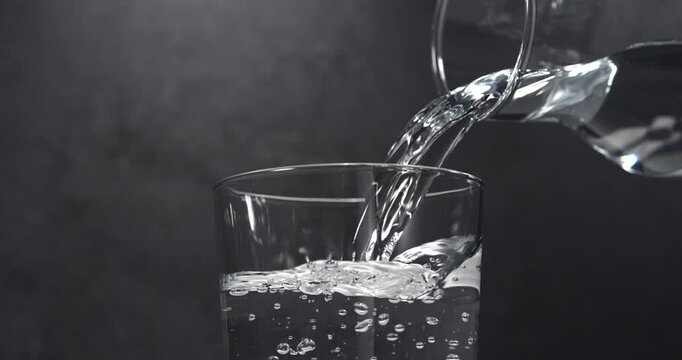 Water pouring from pitcher into glass with ice in slow motion