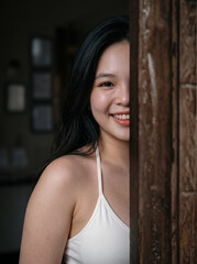 Fototapeta premium Smiling woman peeking from behind wooden doorway