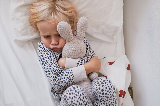 Upset little girl hugging knitted bunny toy in bed