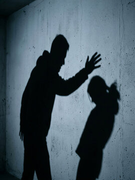 Man threatening girl&rsquo;s silhouette on a wall in a dimly lit room  