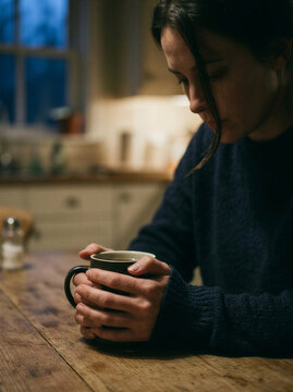 Young woman holding a cup of coffee at a wooden table indoors  