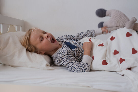 Angry little girl crying and throwing stuffed toy in bed