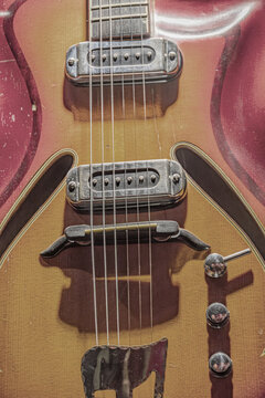 Close-up view of vintage electric guitar, showcasing sunburst finish, detailed wood grain, semi-hollow body design, six-string setup, metal bridge and tuning pegs, in soft even lighting, top-down