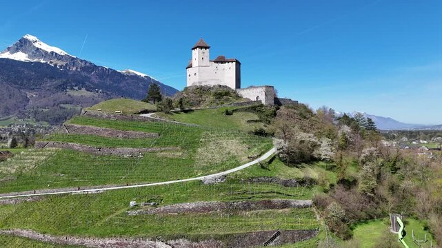 gutenberg castle hilltop tower stone walls vineyard terraces steep hillside drone aerial orbit snowcapped alpine peaks mountain range green valley farmland liechtenstein rhine valley heritage site