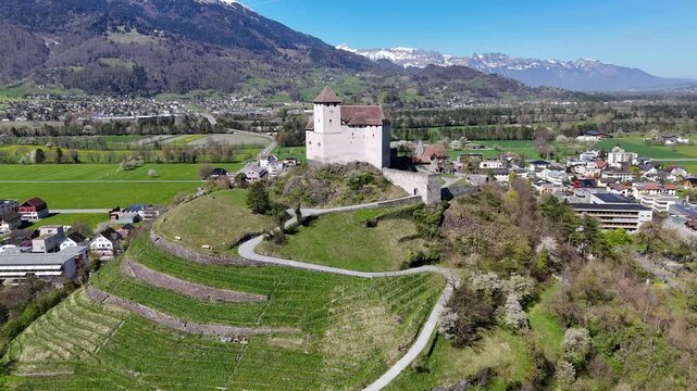 gutenberg castle hillside fortress stone tower balzers rooftops drone aerial orbit alpine peaks mountain range green valley farmland modern buildings liechtenstein rhine valley heritage site