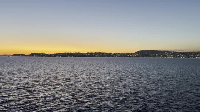27 April 2026 Italy, Campania, Gulf of Naples - sail away cruising alongside Mainland to Messina during sunset with beautiful city skyline lights