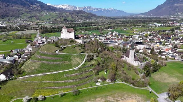 hilltop castle balzers liechtenstein establishing shot round tower parish church terraced vineyard slopes town rooftops rhine valley farmland snowcapped alpine peaks drone footage travel destination