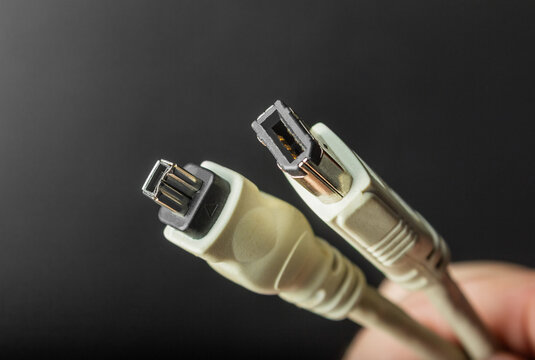 Photo of a hand holding firewire sound board input cables on black background.
