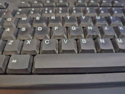 Close-up of a dusty black computer keyboard with worn keys and visible particles