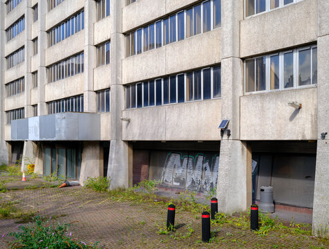 Disused concrete office block located on a quiet street in Aberdeen showing clear signs of neglect with overgrown weeds and weathered glass windows