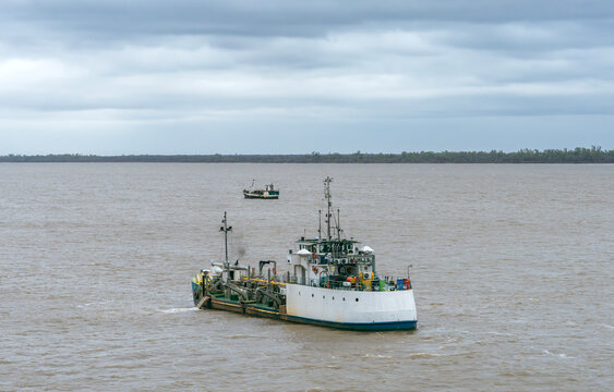 Small dredger vessel navigating open water under an overcast sky, showing maritime industrial operations, equipment, deck details, and water transport on a cloudy day