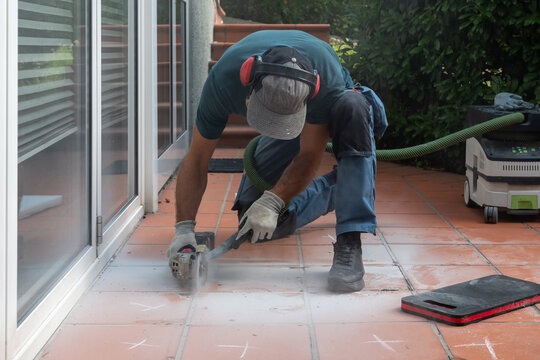 Worker cutting patio tiles with angle grinder on outdoor terrace