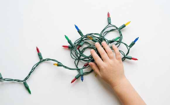 Child touching a tangled pile of colorful Christmas string lights on a white background