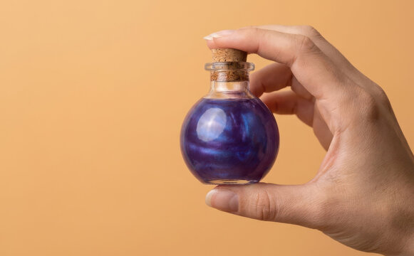 Hand holding a magical purple potion in a glass bottle with cork stopper representing fantasy and mystery