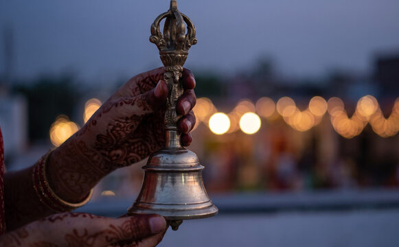 Woman holding a traditional brass ritual bell during a religious ceremony with bokeh lights