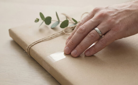 Man packaging a book wrapped in brown paper with twine and eucalyptus branch for delivery