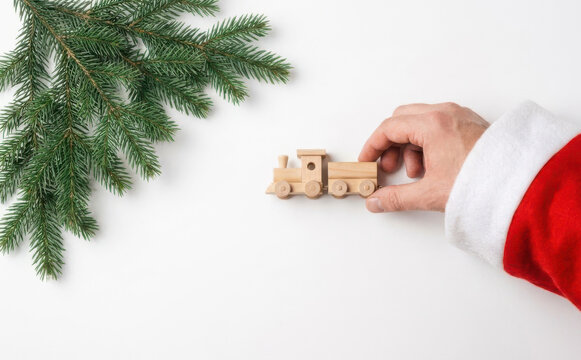 Santa Claus holding a wooden toy train near pine branches for Christmas holiday gift concept