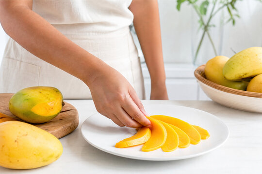 Woman plating freshly sliced ripe yellow mangoes on white plate