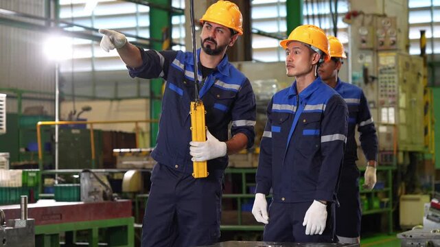 Group of industrial engineers wearing safety helmets and uniforms collaborating and pointing forward in factory, Factory workers discussing production line and operating machinery in industrial plant