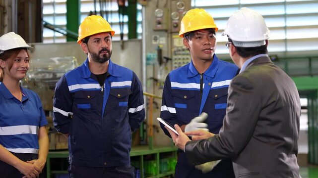 Industrial team and manager wearing safety helmets discussing report on tablet in factory, professional engineers and workers talking and planning production line with supervisor in industrial plant