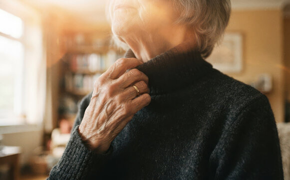 Elderly woman in black turtleneck sweater touching her neck indoors, senior care and health concept