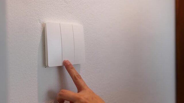 Close up video of a person turning on and off the light with a switch in a modern home, showcasing daily energy usage.